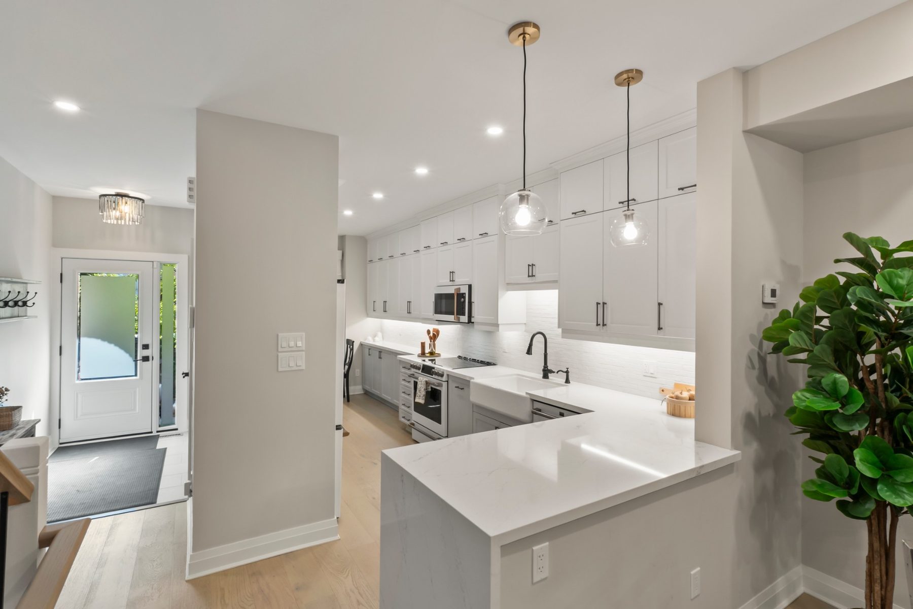 Renovated kitchen with white shaker cabinets to the ceiling, quartz waterfall peninsula, farmhouse sink and GE Café appliances