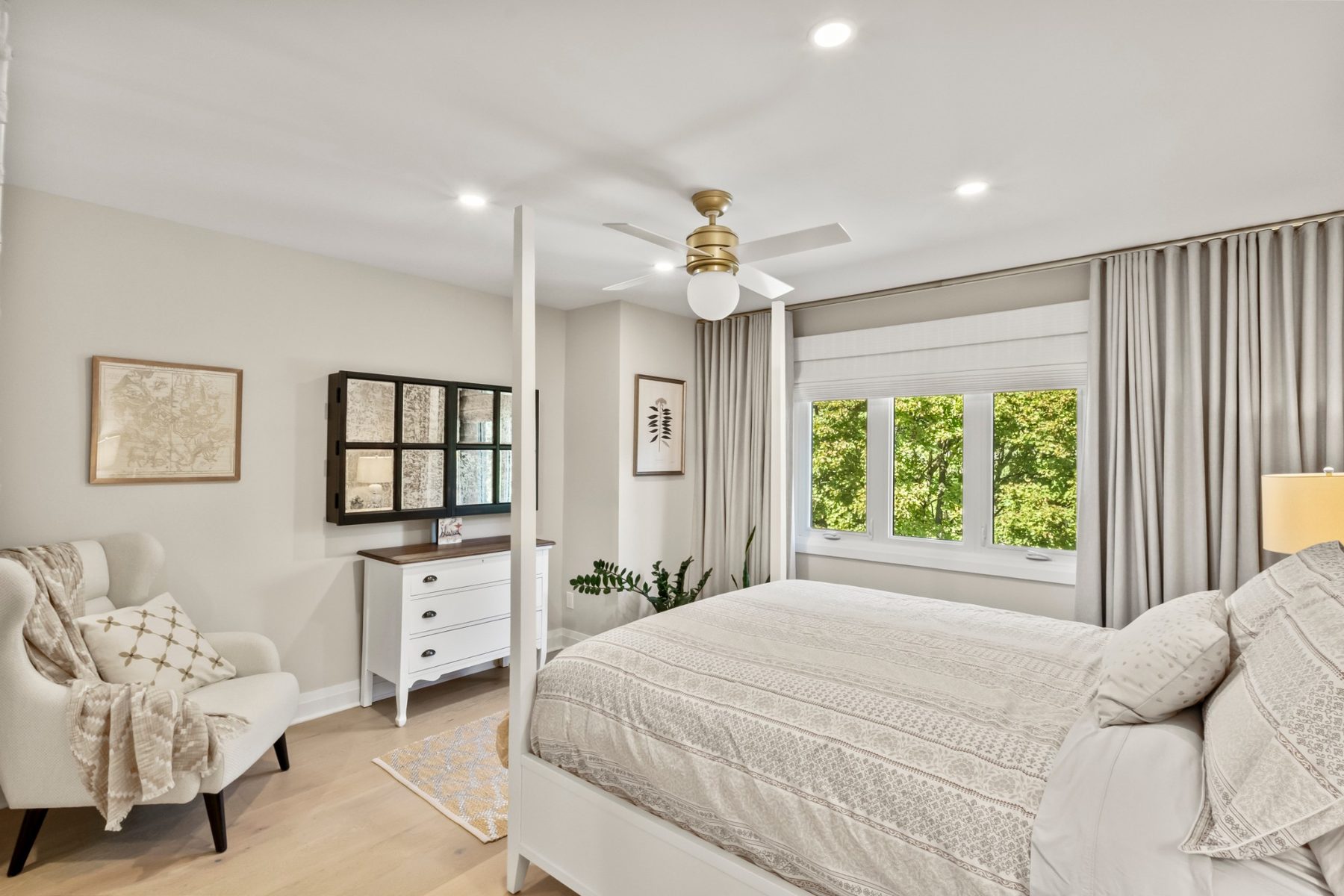 Primary bedroom with hardwood floors, ceiling fan and a wide window onto the trees